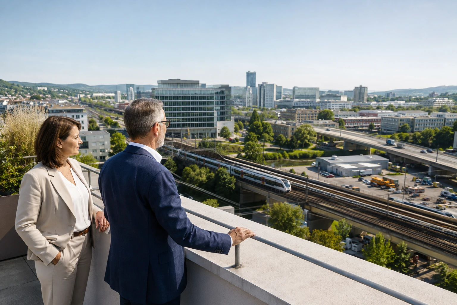 Zwei Personen auf einer Terrasse mit Blick auf Bürogebäude und Verkehrsanlagen